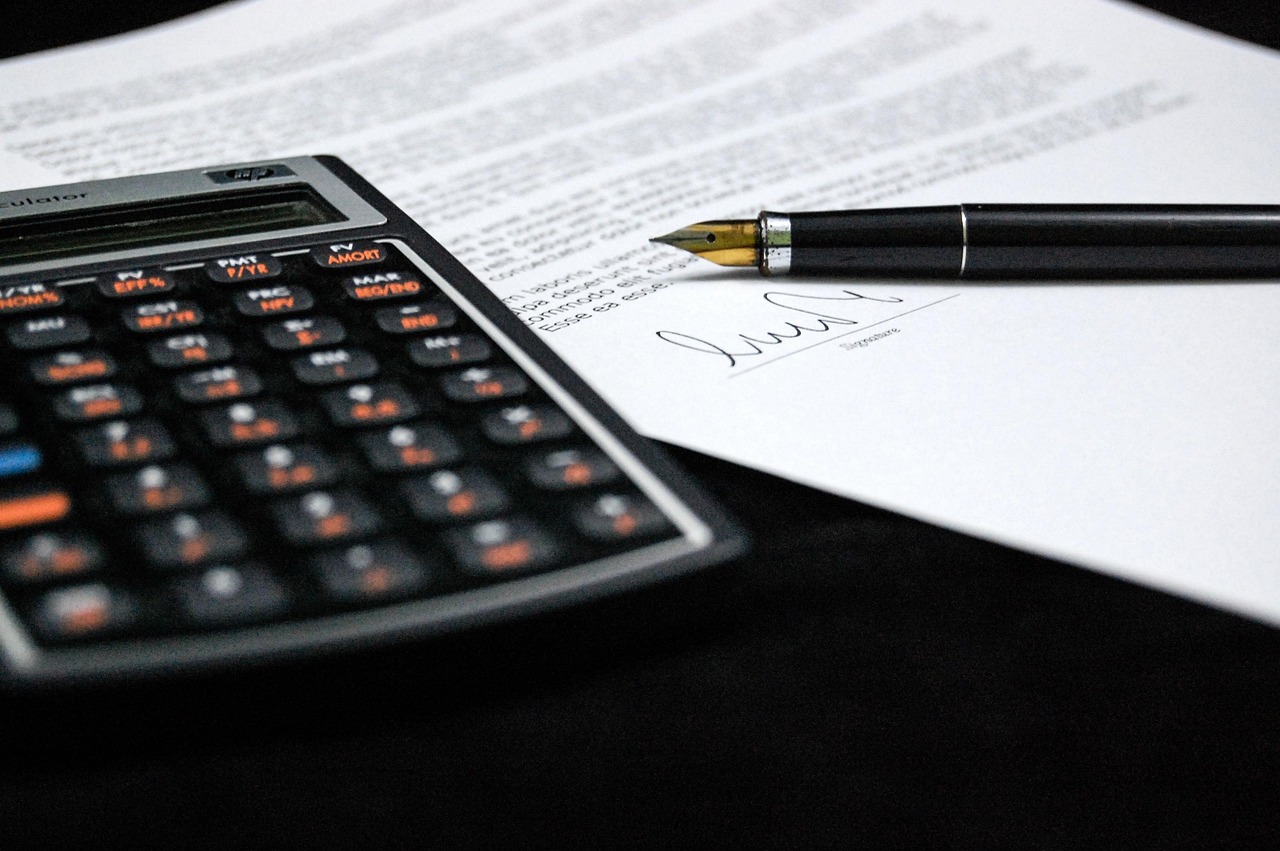 Legal contract documents, house keys, and financial calculator arranged on a wooden desk.