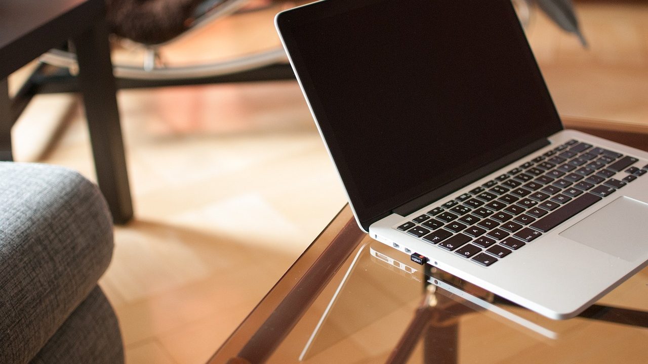A laptop open on a clean wooden desk with a notebook and pen next to it.