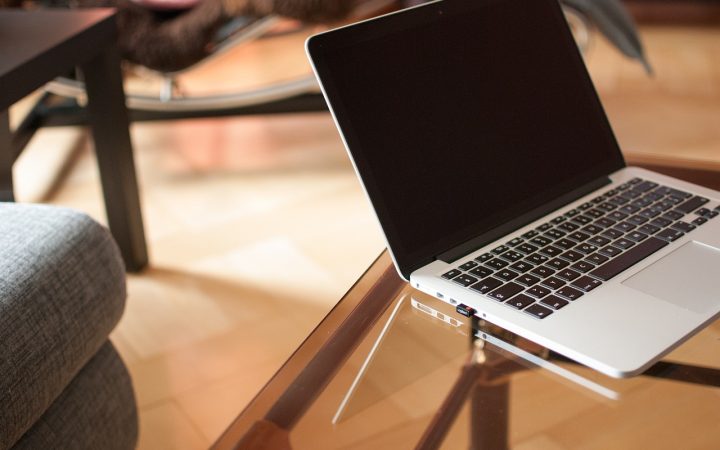 A laptop open on a clean wooden desk with a notebook and pen next to it.