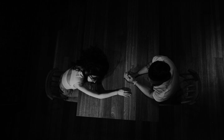An engaged couple sitting at a wooden table reviewing financial documents together on a laptop in a brightly lit room.