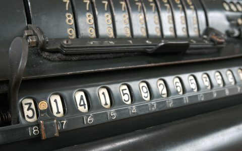 An eighth grade student reviewing math notes and a calculator at a wooden school desk.