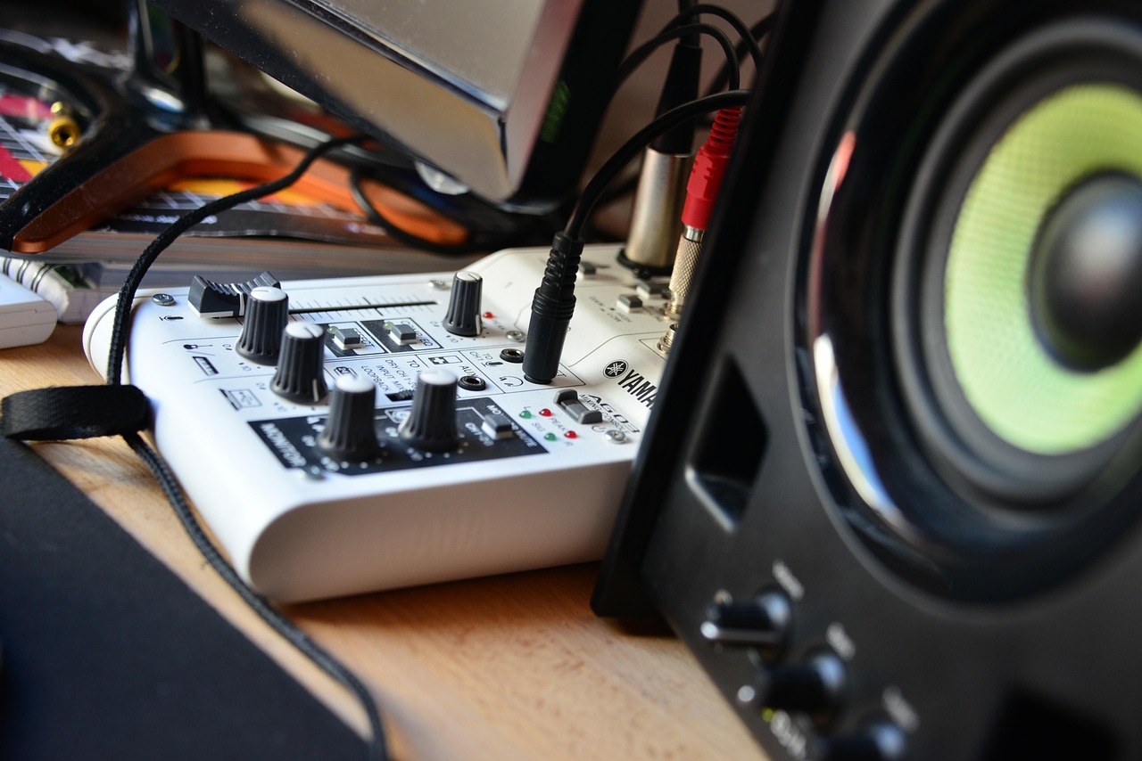 Hardware audio mixer with faders and knobs sitting on a home office desk.