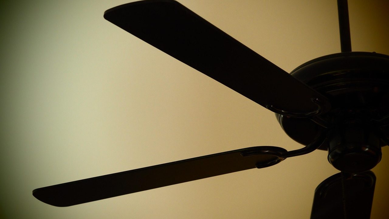 Measuring ceiling fan blade height against ceiling to check balance and alignment.