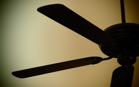 Measuring ceiling fan blade height against ceiling to check balance and alignment.
