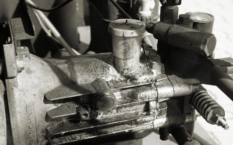 A service technician examining the mechanical compressor compartment behind a modern kitchen refrigerator.
