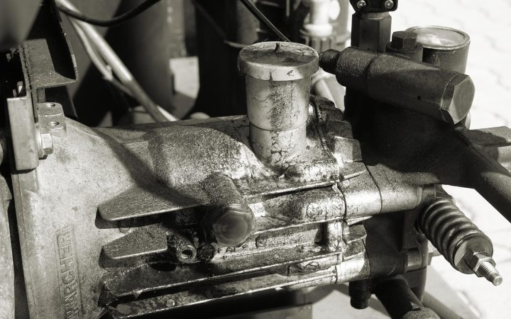 A service technician examining the mechanical compressor compartment behind a modern kitchen refrigerator.