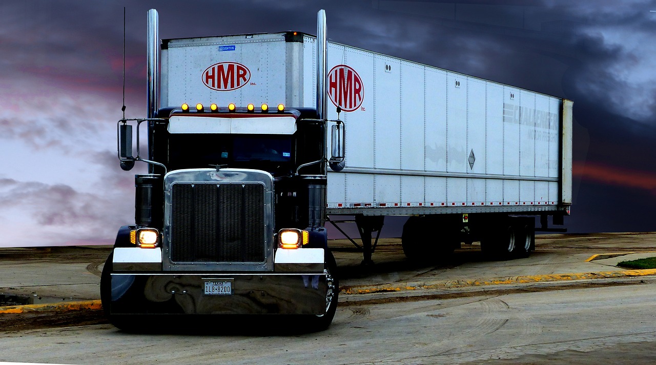 A freight delivery truck unloading a pallet of boxed flooring in a suburban driveway.