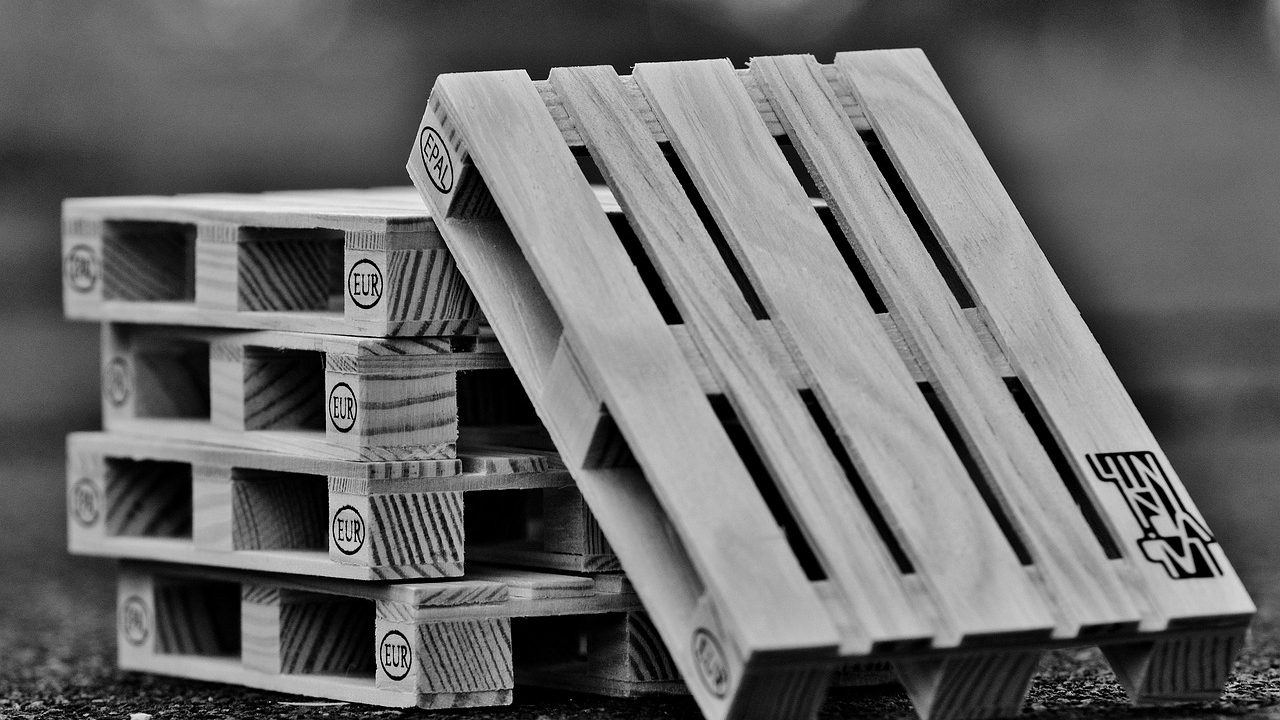 Stacked plastic-wrapped merchandise pallets resting on wooden skids inside a spacious logistics warehouse.