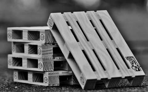 Stacked plastic-wrapped merchandise pallets resting on wooden skids inside a spacious logistics warehouse.