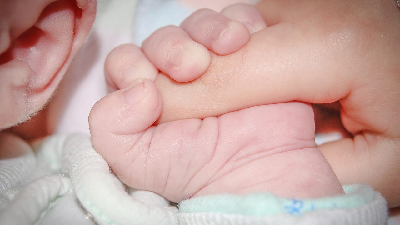 A parent holding a child's hand in a medical clinic waiting area while speaking with a healthcare professional.