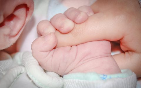 A parent holding a child's hand in a medical clinic waiting area while speaking with a healthcare professional.