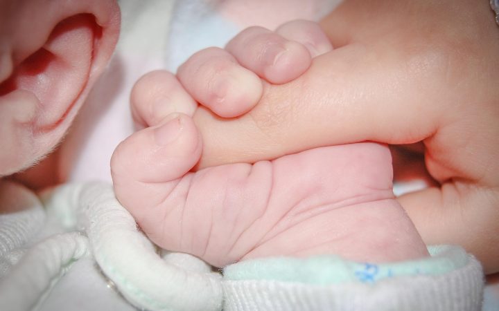 A parent holding a child's hand in a medical clinic waiting area while speaking with a healthcare professional.