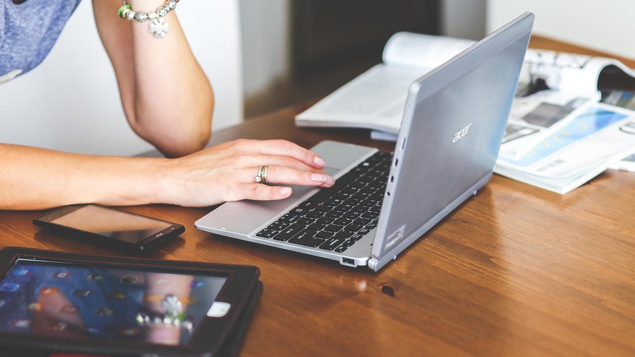 A professional typing notes on a laptop keyboard at a wooden desk.