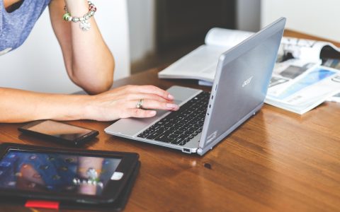 A professional typing notes on a laptop keyboard at a wooden desk.