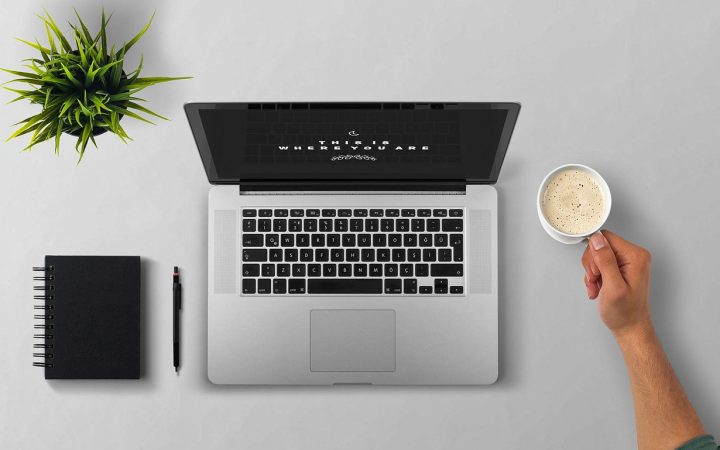 Minimalist modern desk setup with a open laptop, notebook, and ceramic coffee mug bathed in natural light.