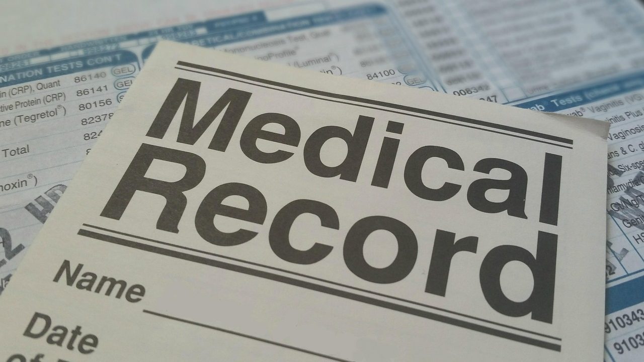 A pet owner reviewing veterinary medical records and policy documents beside their golden retriever at a wooden table.