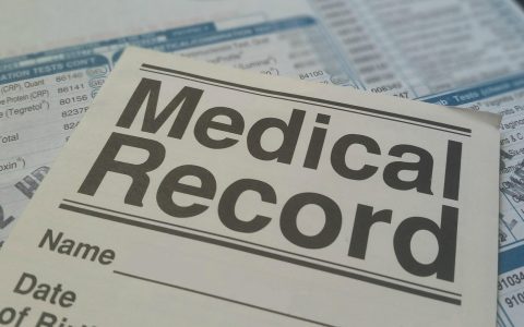 A pet owner reviewing veterinary medical records and policy documents beside their golden retriever at a wooden table.