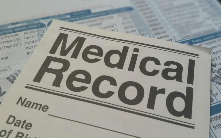 A pet owner reviewing veterinary medical records and policy documents beside their golden retriever at a wooden table.