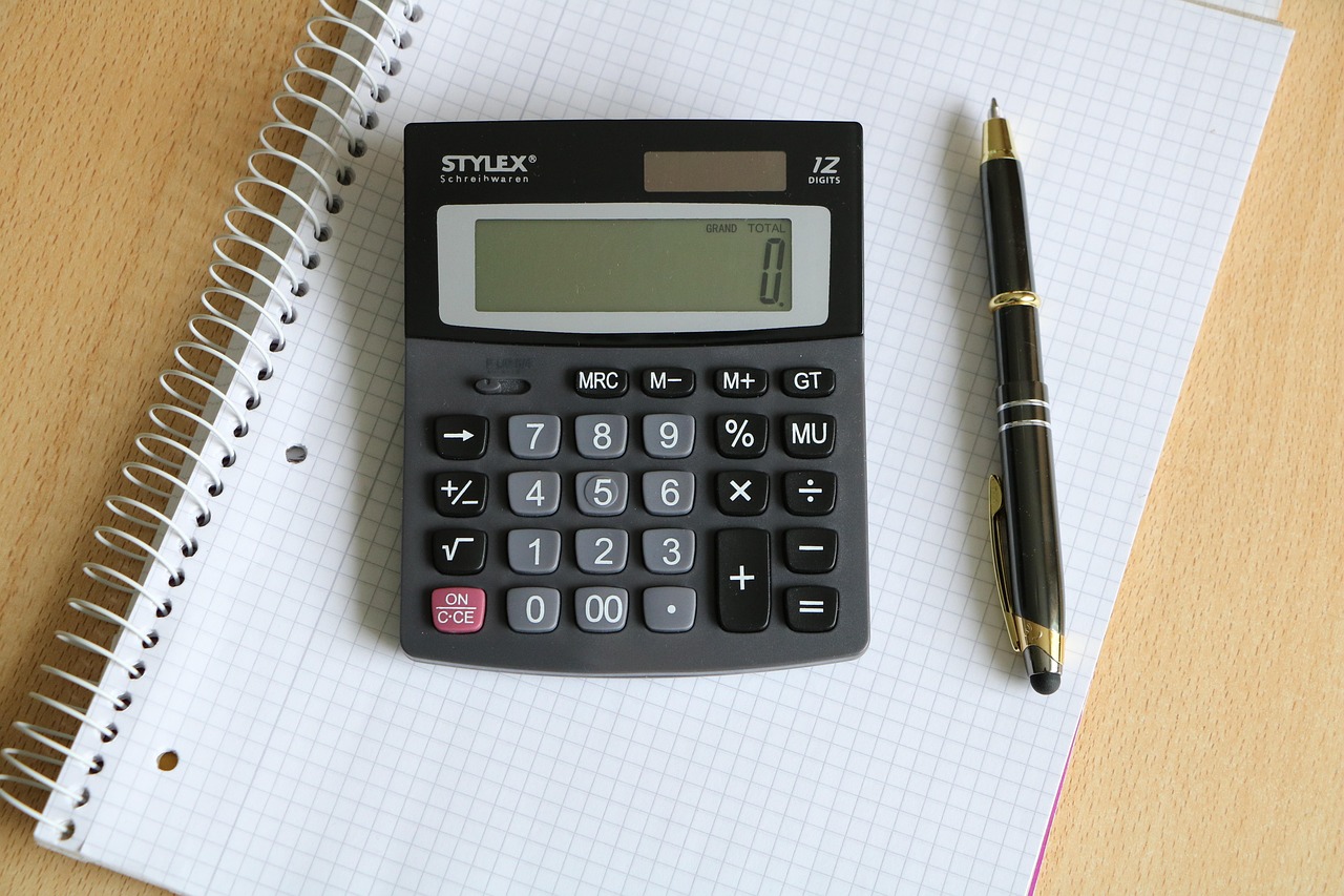 A calculator, pen, and utility statements on a desk prepared for a household bill audit.