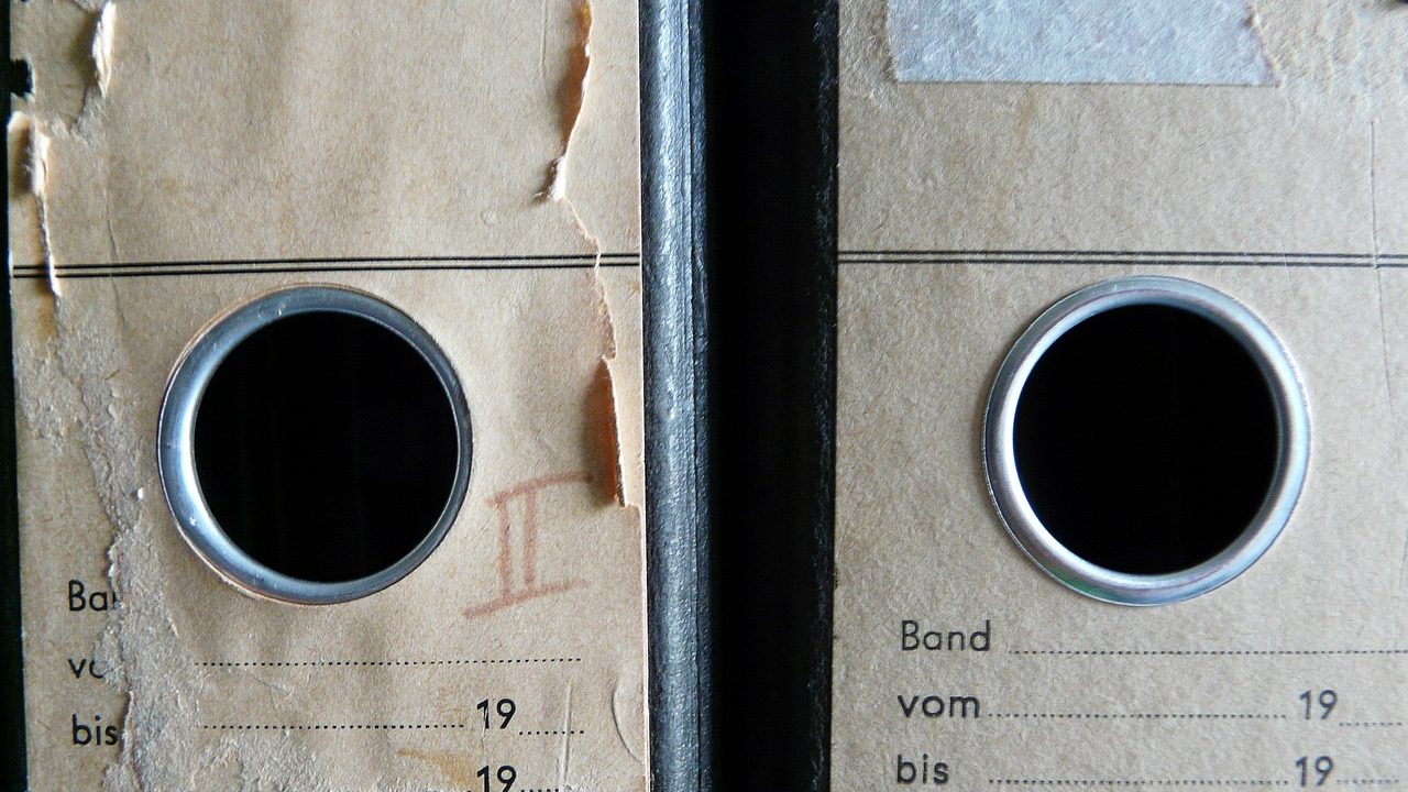 A person organizing physical and digital files on a wooden desk.