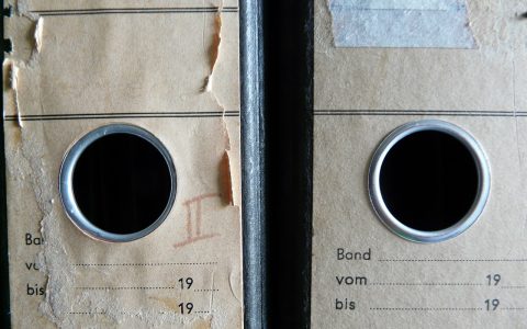 A person organizing physical and digital files on a wooden desk.