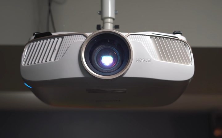 A person adjusting a ceiling-mounted home theater projector in a media room.