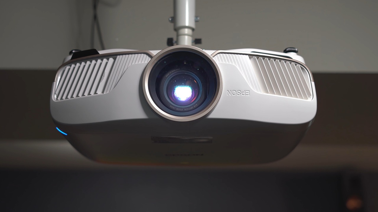 A person adjusting a ceiling-mounted home theater projector in a media room.