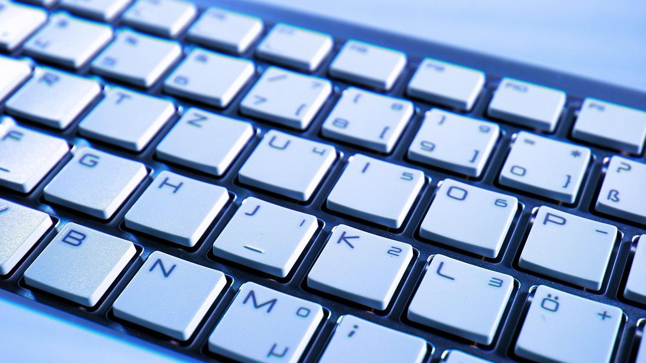 Close-up of hands typing on a modern mechanical keyboard at a wooden desk.