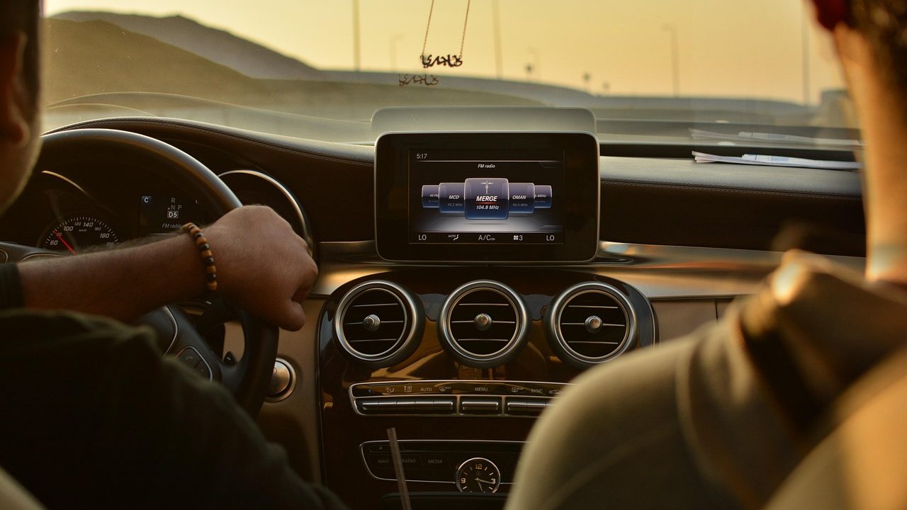 A driver side interior of a car at night showing a smartphone mounted on the dashboard with a map route app visible.