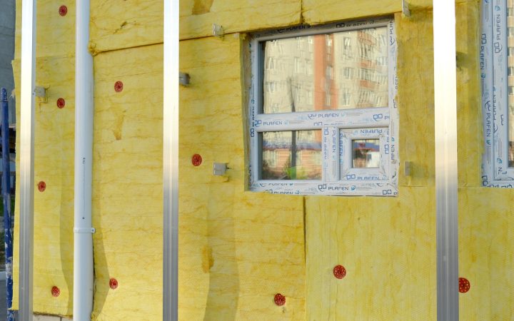 Homeowner installing rigid foam insulation board into a basement rim joist cavity and sealing edges with spray foam.