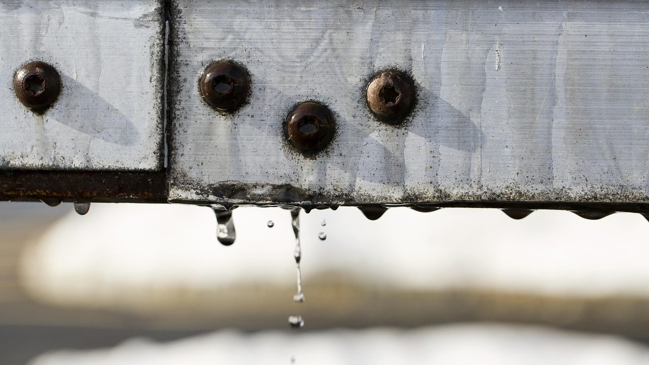 Close-up of installed metal drip edge flashing under asphalt roof shingles above seamless gutters.