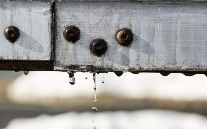 Close-up of installed metal drip edge flashing under asphalt roof shingles above seamless gutters.