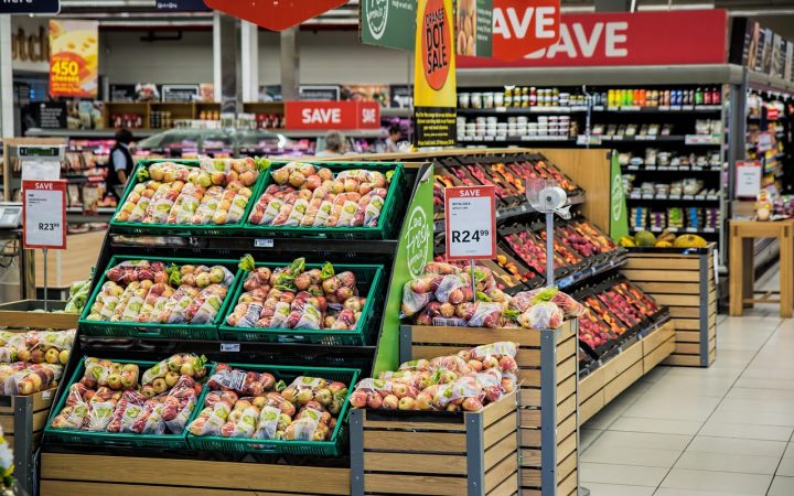 Shopper pushing a cart down a supermarket grocery aisle filled with food products.
