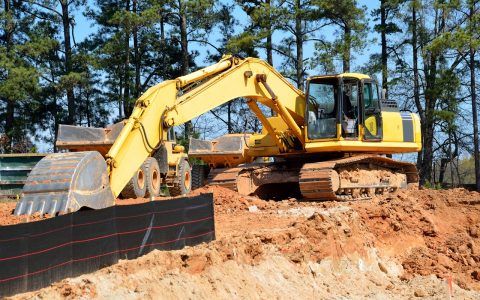 Backhoe excavator parked near an open soil trench during a residential septic system inspection.