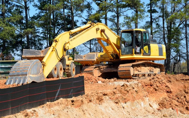 Backhoe excavator parked near an open soil trench during a residential septic system inspection.