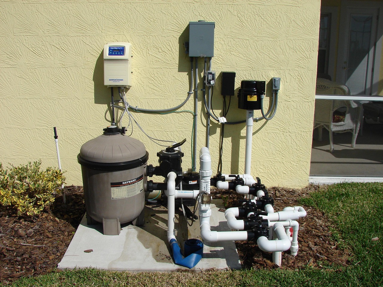 An outdoor heat pump condenser unit installed along the side foundation wall of a suburban house.