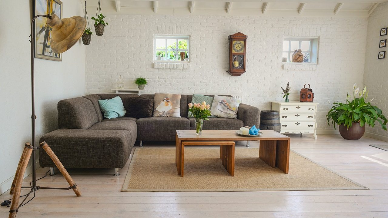 Close-up of a modern residential floor vent register in a sunlit living room with natural hardwood flooring.