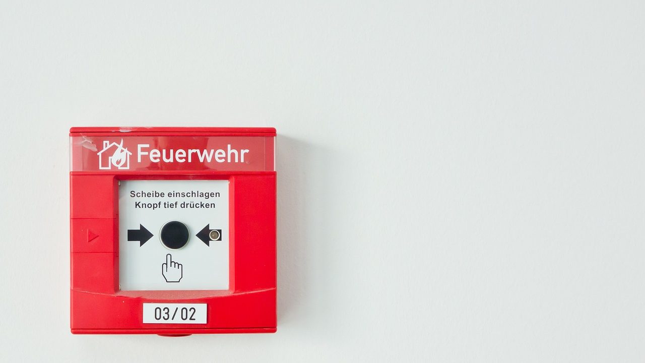 Homeowner pressing the test button on a ceiling smoke detector using a broom handle.