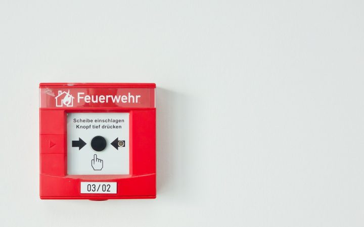 Homeowner pressing the test button on a ceiling smoke detector using a broom handle.