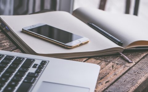 Parent organizing summer camp schedules and finances on a laptop and paper calendar at home.