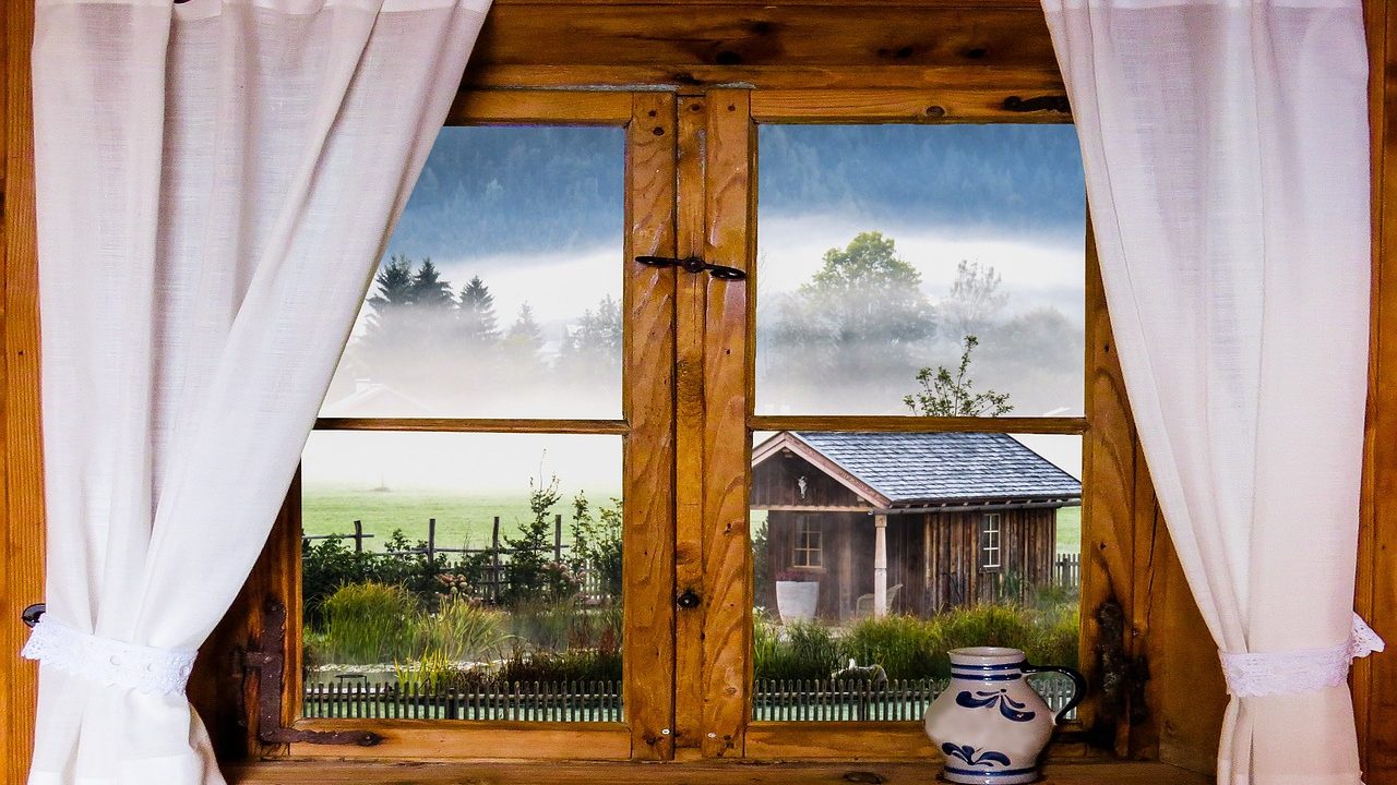 A person adjusting heavy fabric curtains over a living room window during winter.