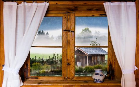 A person adjusting heavy fabric curtains over a living room window during winter.