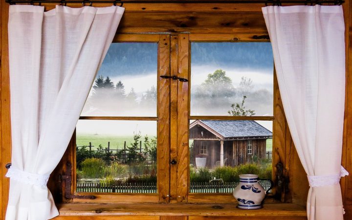 A person adjusting heavy fabric curtains over a living room window during winter.