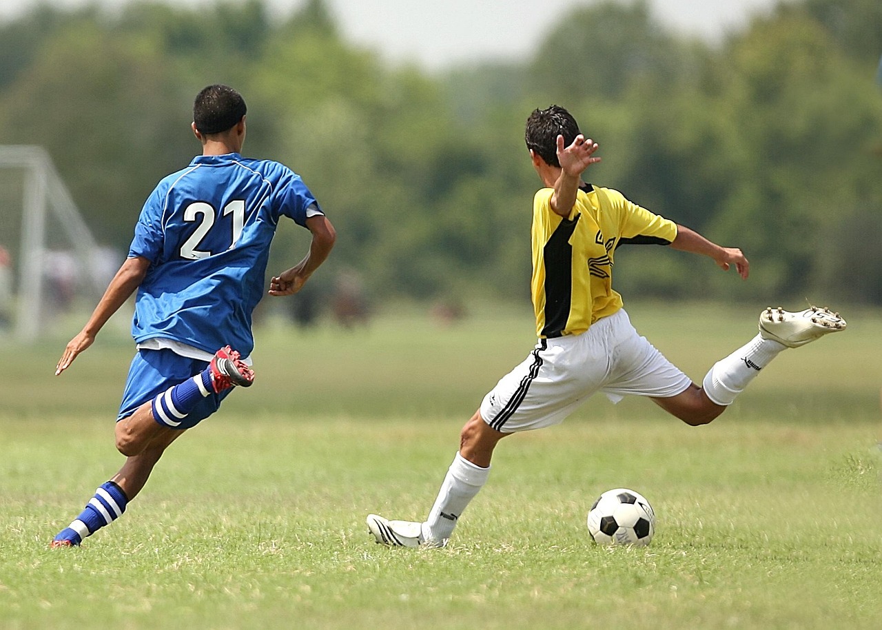 Parent budgeting household expenses on a laptop with soccer uniforms nearby.