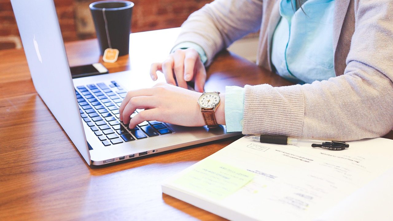 A laptop showing a secure digital document portal alongside physical mail and office accessories on a wooden desk.