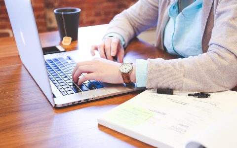 A laptop showing a secure digital document portal alongside physical mail and office accessories on a wooden desk.