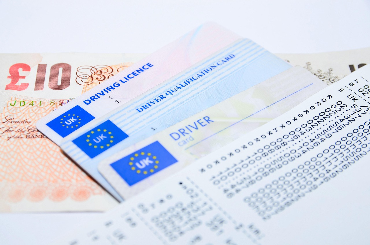 A person holding a state driver's license in front of a home office setup.
