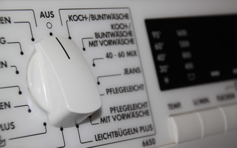Front-load washing machine with stainless steel drum open in a modern laundry room.