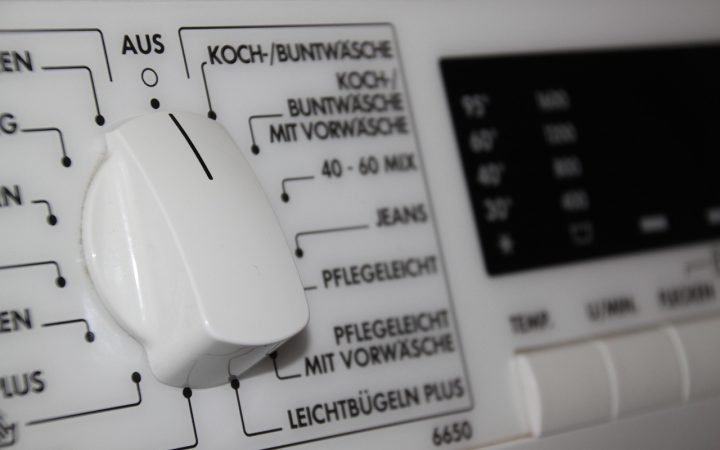 Front-load washing machine with stainless steel drum open in a modern laundry room.