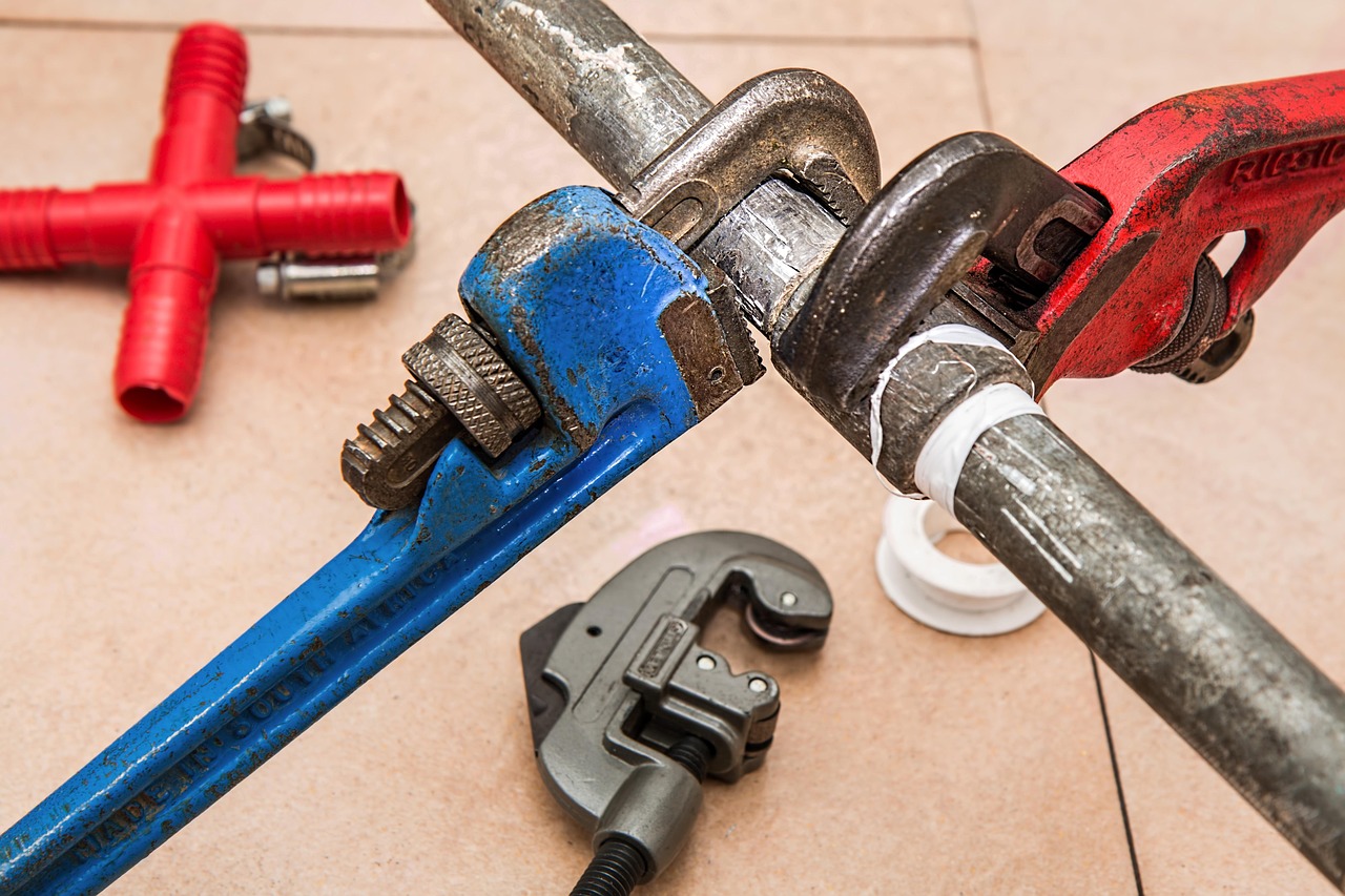Plumber holding pipe wrenches next to residential water heater